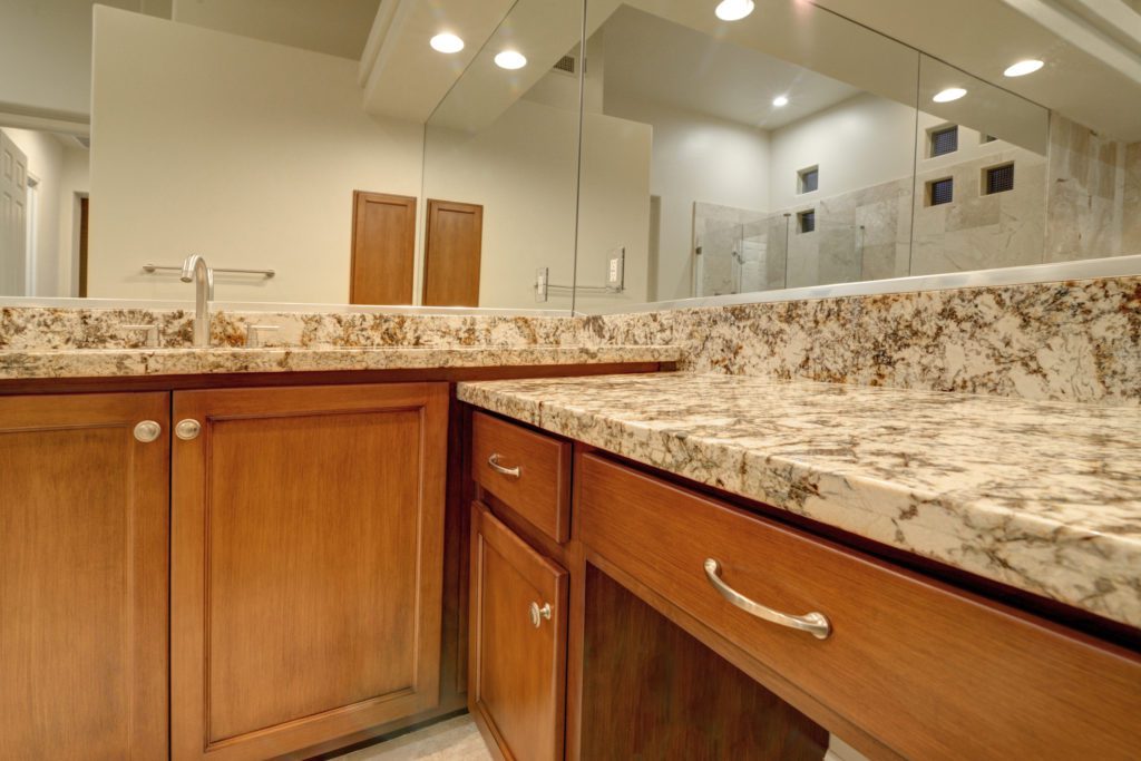 A bathroom with marble counter tops and wooden cabinets.