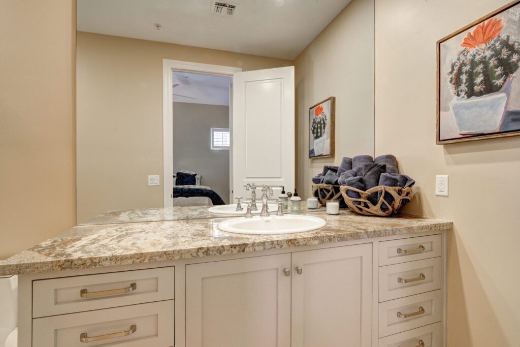 A bathroom with marble counter tops and white cabinets.