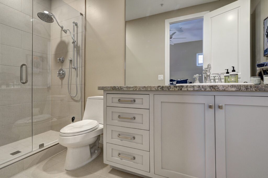 A bathroom with white cabinets and marble counter tops.