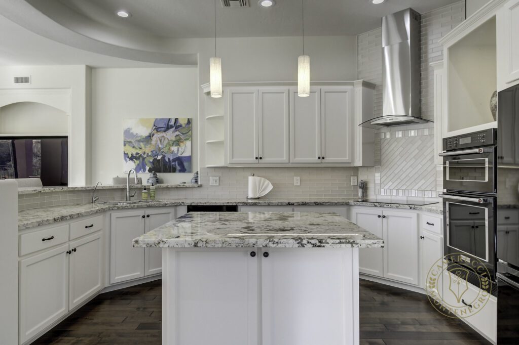 A kitchen with white cabinets and marble countertops.