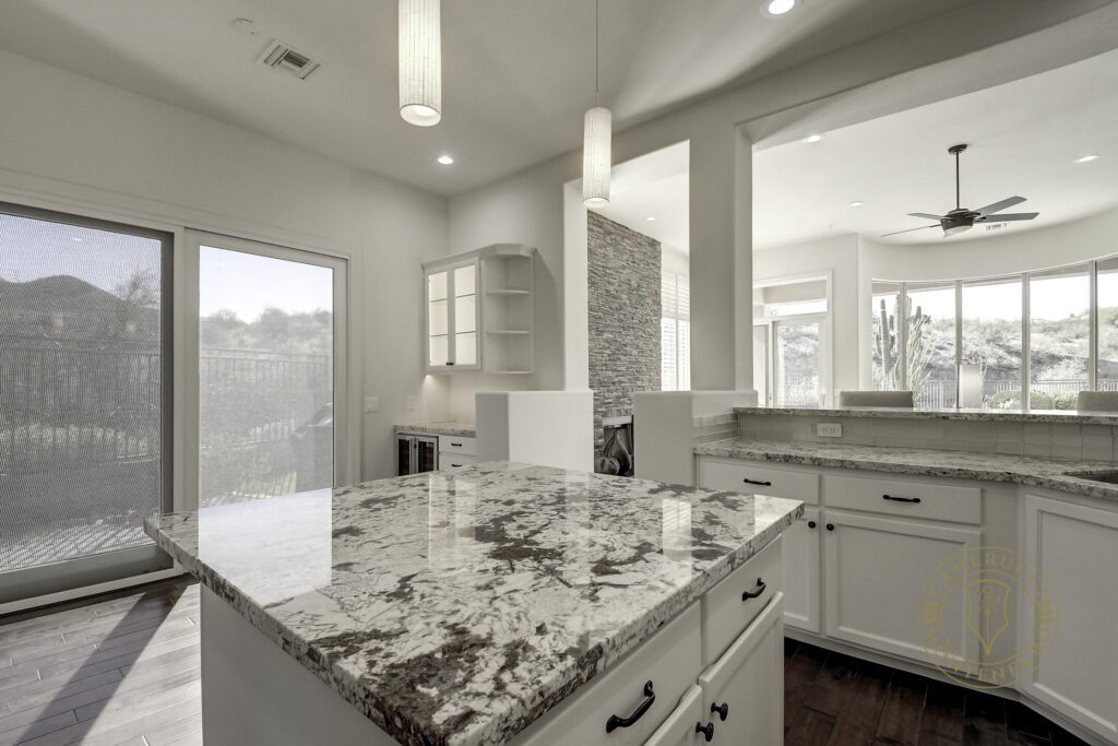 A kitchen with white cabinets and marble counter tops.
